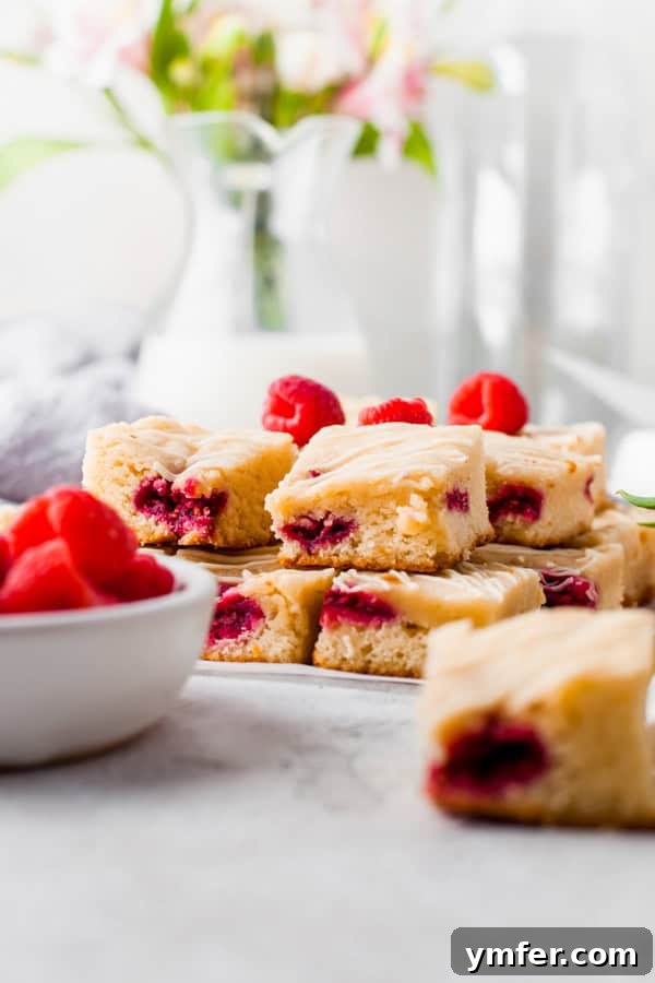 Ruby Raspberry Blondies 5 Several white chocolate raspberry blondies stacked on a table, ready to be served.