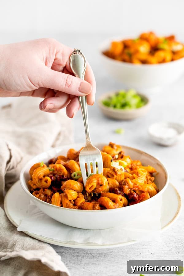 Hearty Instant Pot Chili Mac 5 A fork taking a spoonful of cheesy chili mac from a white bowl.