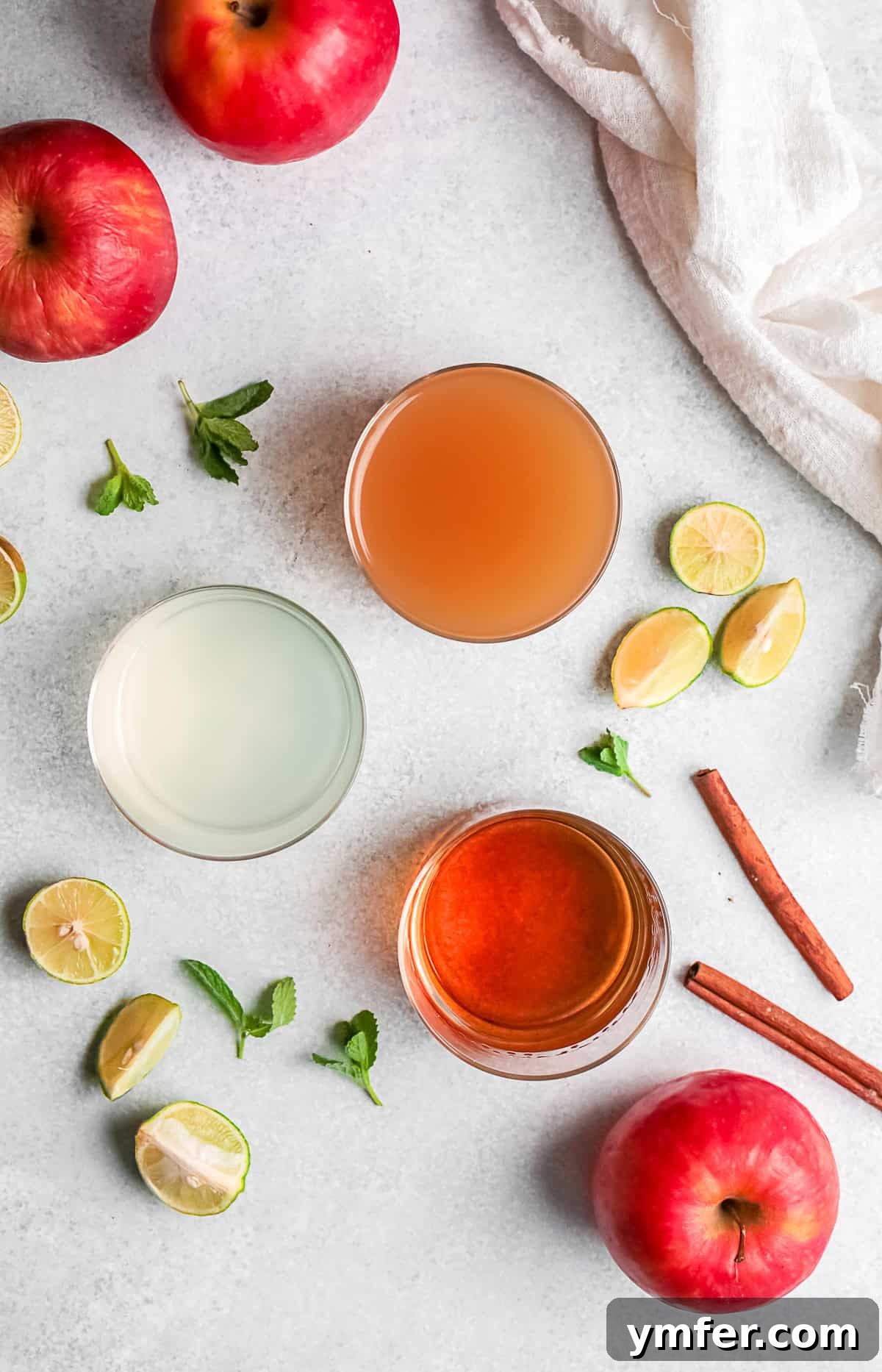 Various ingredients for an apple cider mojito, including a bottle of rum, fresh limes, mint sprigs, and a jug of apple cider, artfully arranged on a rustic table.