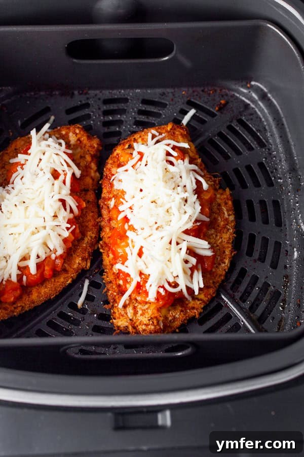 Crispy Air Fryer Chicken Parmesan 4 Crispy chicken cutlets in an air fryer topped with red sauce and cheese, ready to be cooked further.