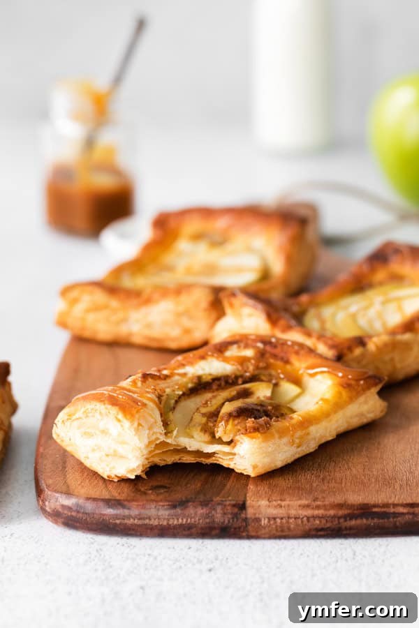 Gooey Apple Caramel Pastry 6 A close-up of a warm caramel apple danish with a bite taken, showcasing the flaky pastry layers and the sweet, tender apple filling inside.