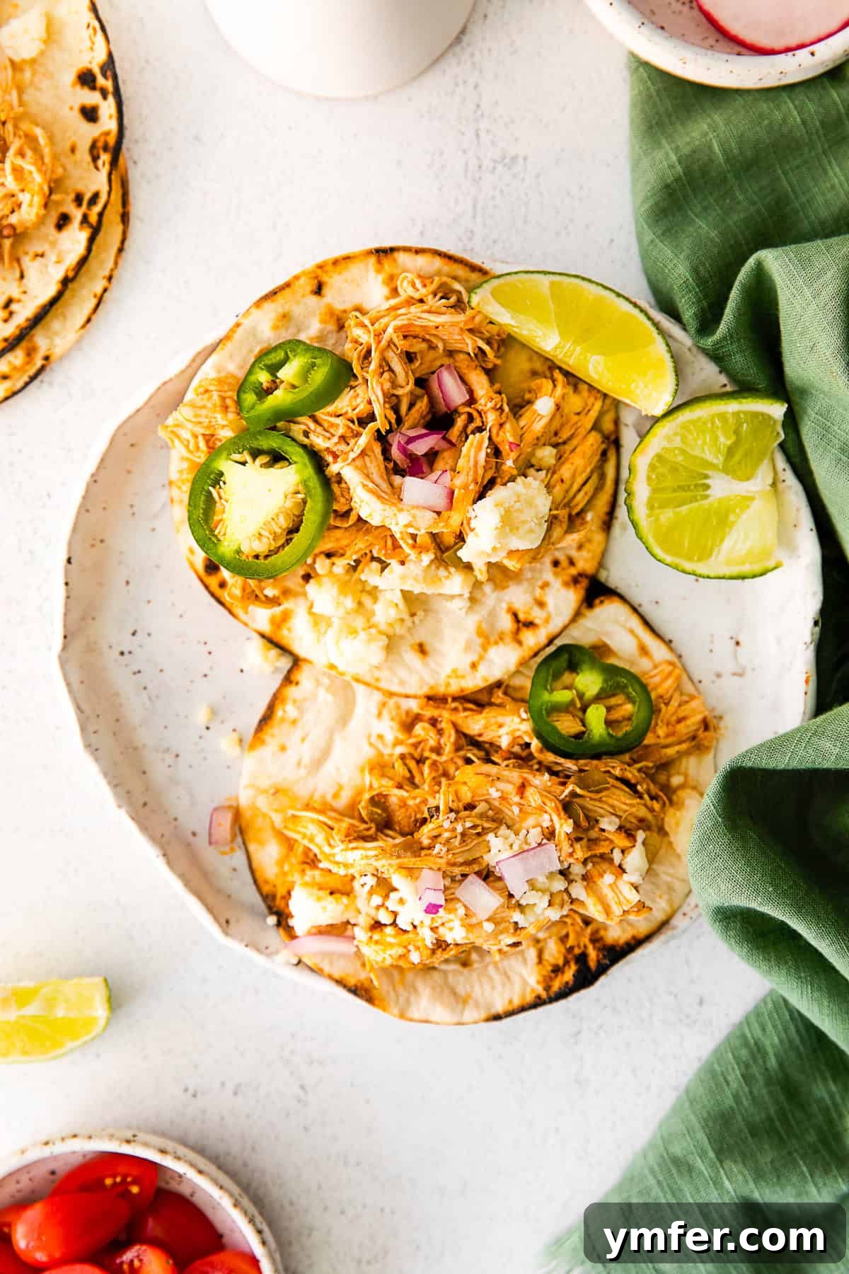 Effortless Instant Pot Chicken Tacos 2 Instant Pot Chicken Tacos on a white plate, garnished with fresh cilantro and a lime wedge.