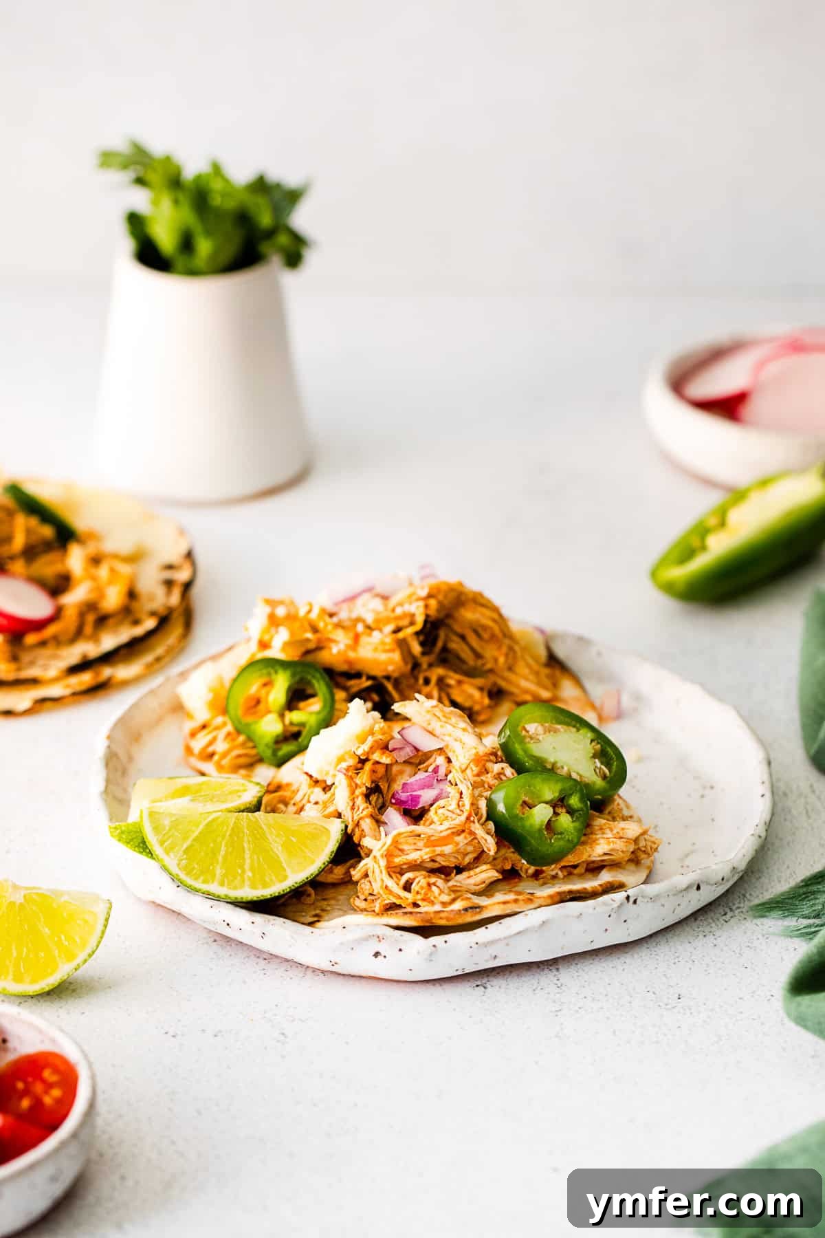 Effortless Instant Pot Chicken Tacos 10 Two Instant Pot Chicken Tacos generously topped with shredded cheese, diced red onions, and fresh cilantro, alongside a serving of salsa.