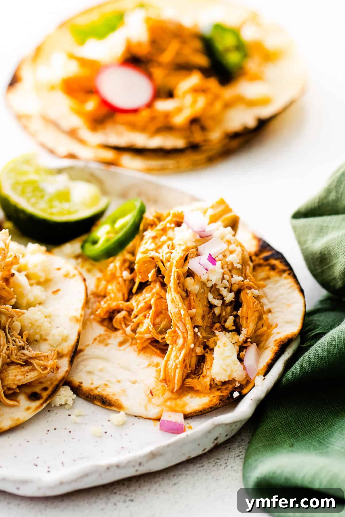 Effortless Instant Pot Chicken Tacos 11 An appetizing close-up of two Instant Pot Chicken Tacos on a white plate, ready to be enjoyed.