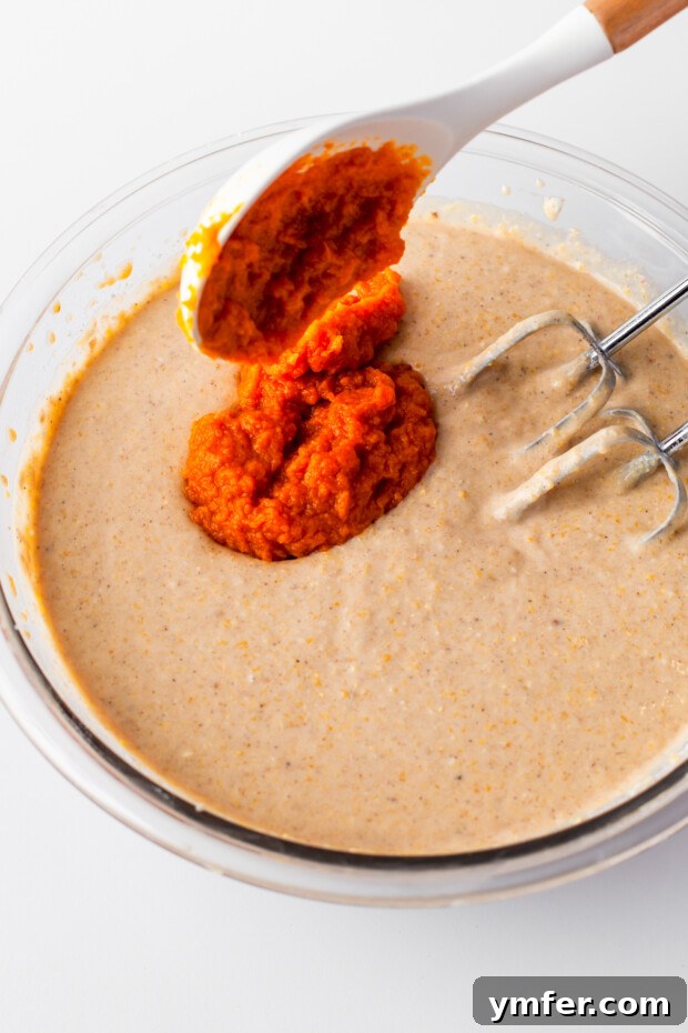 Golden Spiced Pumpkin Cornbread Muffins 4 Fresh pumpkin puree being carefully added to the muffin batter, ensuring even distribution of flavor.