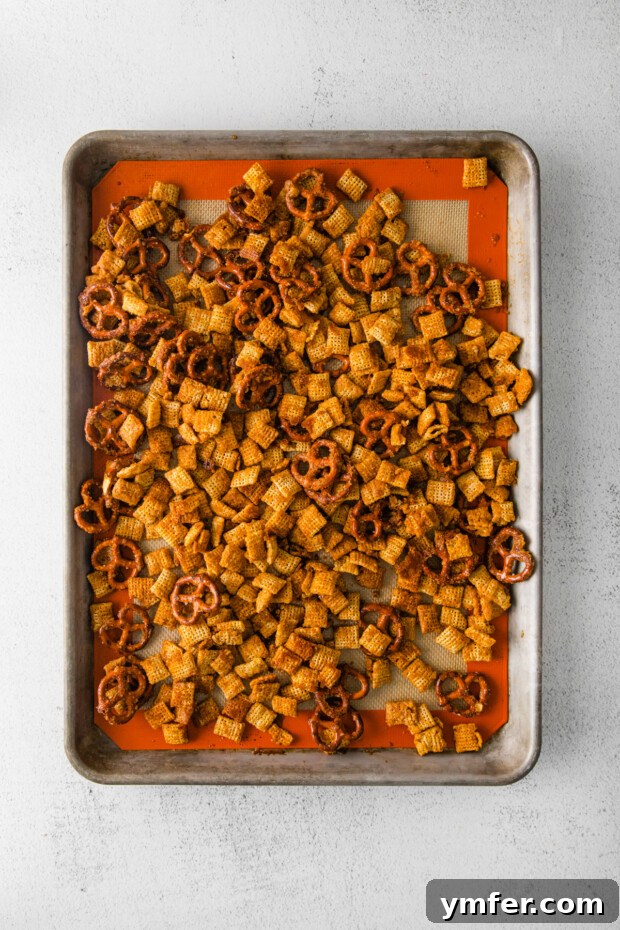 Autumn Snack Crunch 6 Harvest Chex Mix spread in an even layer on a parchment-lined baking sheet, prepared for its time in the oven.