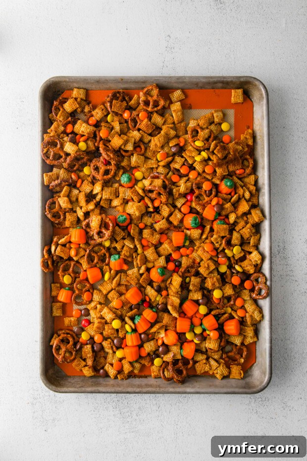 Autumn Snack Crunch 8 Harvest Chex Mix spread on a baking sheet, showcasing its golden-brown glaze and various components before final additions.