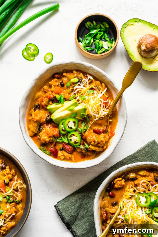 Autumn Harvest Turkey Chili 2 A steaming bowl of Turkey Pumpkin Chili, generously topped with creamy avocado slices, shredded cheese, and vibrant sliced jalapeños, ready to be enjoyed.