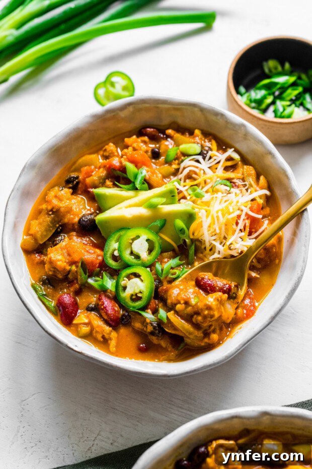 Autumn Harvest Turkey Chili 7 A rustic, deep bowl filled with comforting Turkey Pumpkin Chili, accompanied by a spoon ready for a taste, showcasing the rich, autumnal hues of the dish.