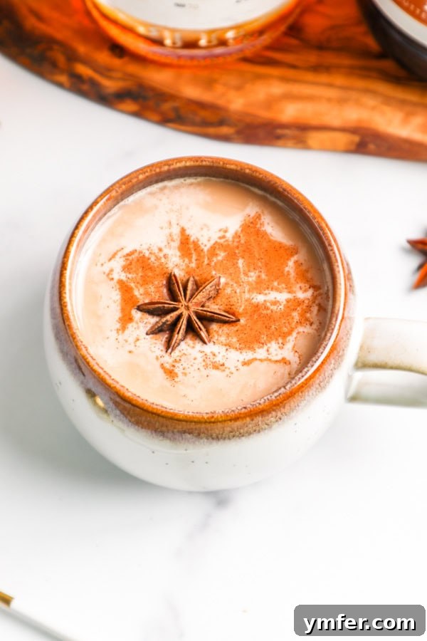 A steaming Skrewball Chai Tea Latte in a ceramic mug, garnished with a sprinkle of cinnamon, sitting on a rustic wooden table.
