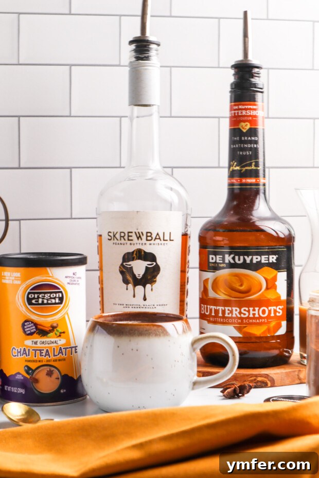 The ingredients for Skrewball Chai Tea Latte laid out on a stylish tiled background, including a bottle of Skrewball whiskey, butterscotch schnapps, and chai tea mix.