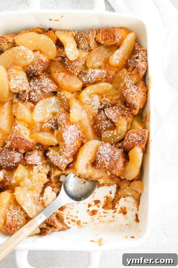 A golden-brown Apple Pie Baked French Toast casserole in a white ceramic baking dish, ready to be served.