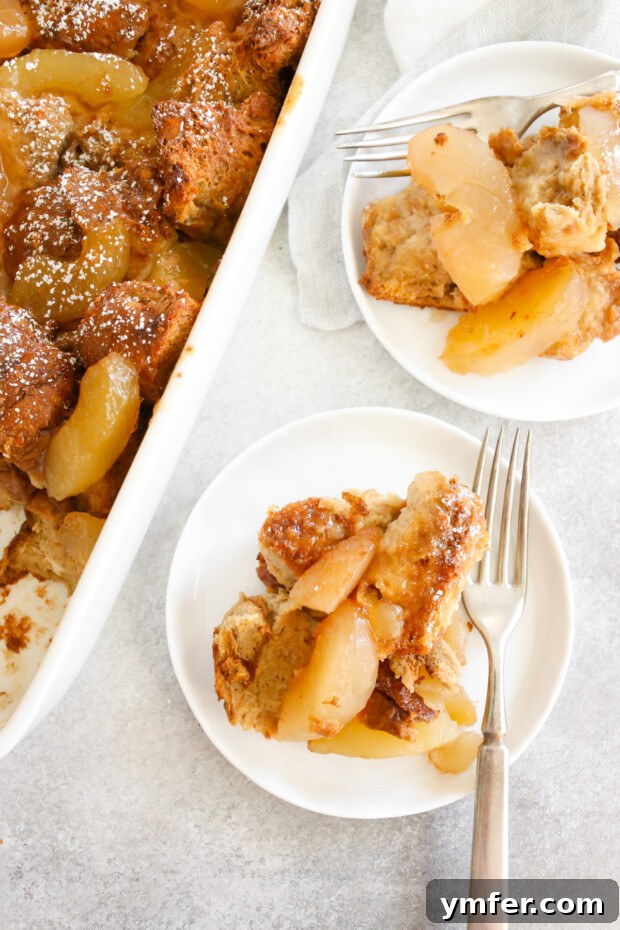 Two individual servings of Apple Pie Baked French Toast, garnished with powdered sugar, resting on small white plates, ready to be enjoyed.