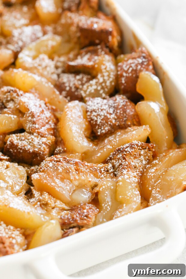 A perfectly baked slice of Apple Pie Baked French Toast, generously topped with a dusting of powdered sugar, waiting to be savored.