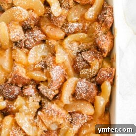A close-up of a square slice of Apple Pie Baked French Toast, showing its golden crust and a hint of apple filling, ready to be served.