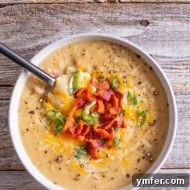 A square image of loaded baked potato soup, topped with bacon, green onions, and cheese.
