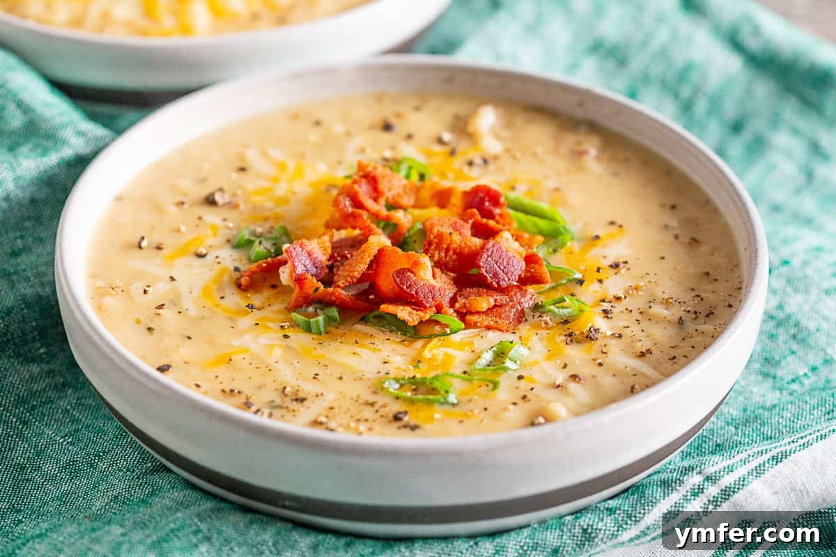 Hearty Loaded Potato Chowder 5 A ceramic bowl filled with creamy loaded baked potato soup, adorned with a variety of classic toppings.