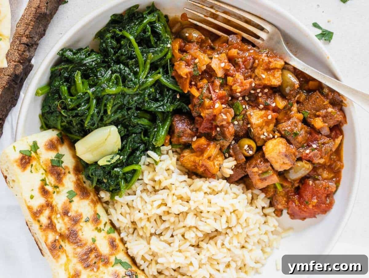 The Forager's Tofu Cacciatore 16 Vegetarian cacciatore artfully presented with fluffy rice, vibrant sautéed kale, and a piece of golden flatbread.