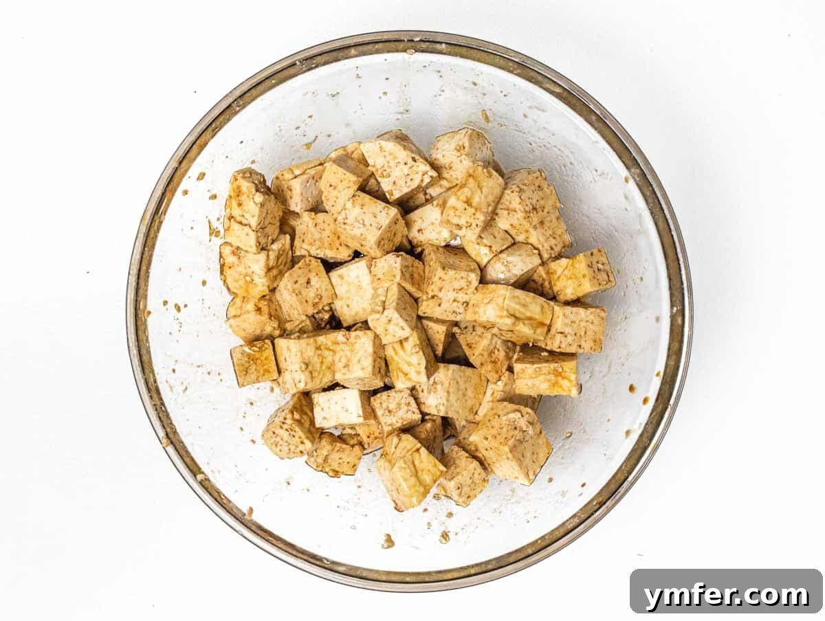 The Forager's Tofu Cacciatore 8 Tofu cubes being seasoned in a bowl with olive oil, soy sauce, and salt, ready to be tossed.