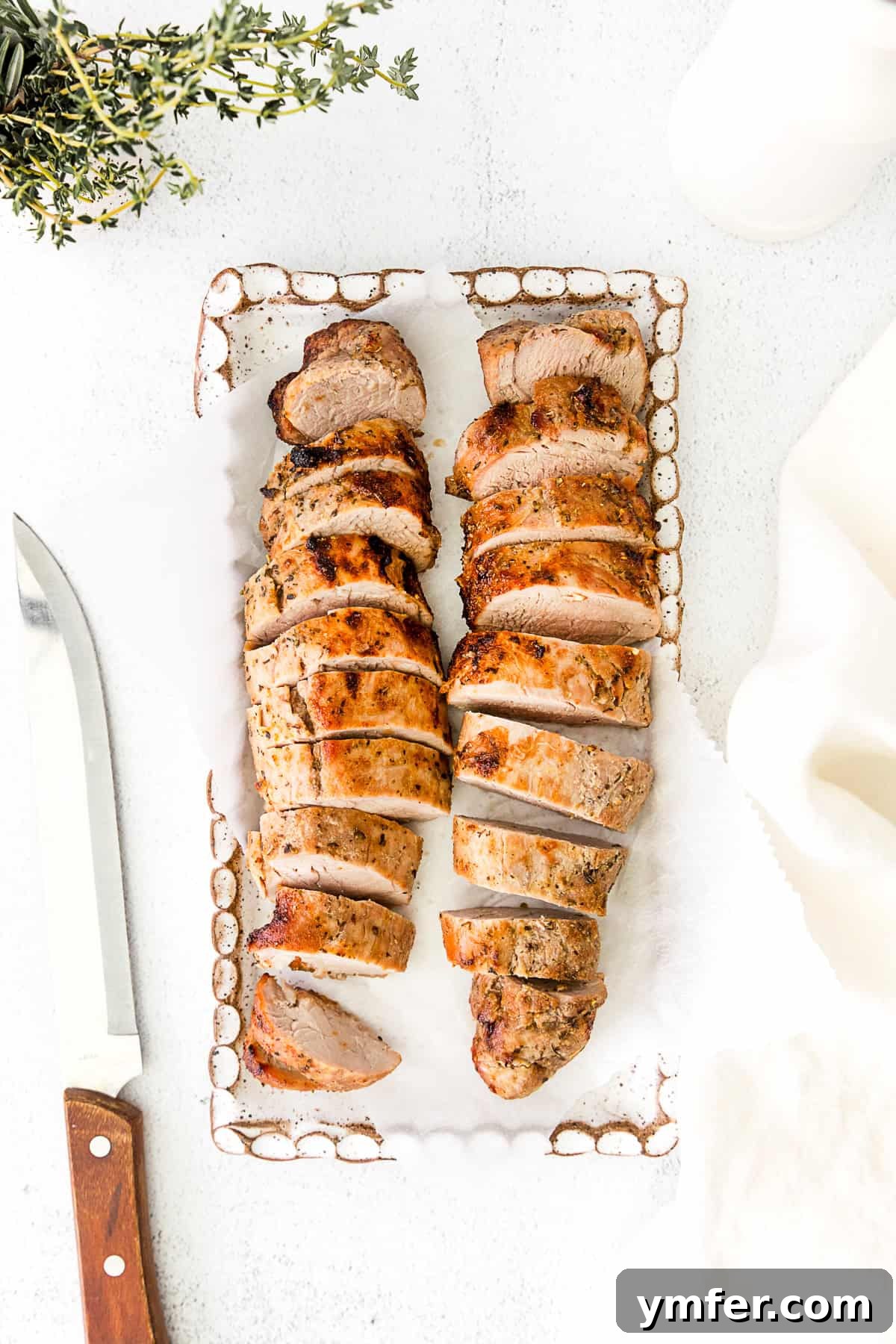 Perfect Air Fryer Pork Tenderloin 2 Air fryer pork tenderloin on a white serving dish, garnished with fresh herbs.