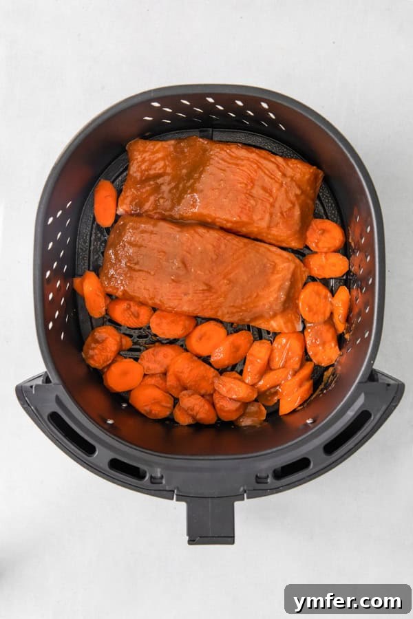 Air Fried Miso-Glazed Salmon 4 Uncooked Air Fryer Miso Salmon with carrots and snow peas arranged in an air fryer basket, ready to cook.