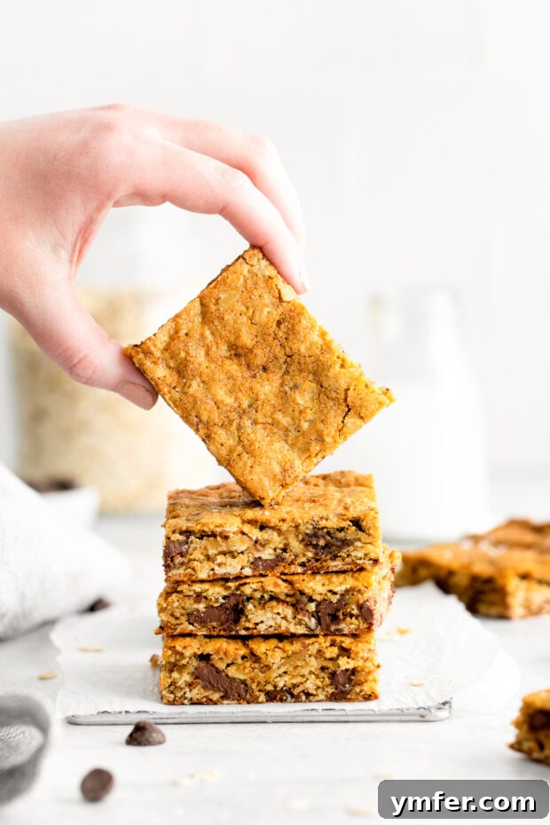 Ultimate Chocolate Chunk Oatmeal Bars 2 Chocolate Chunk Oatmeal Cookie Bars stacked on top of each other, showcasing their chewy texture and melted chocolate.