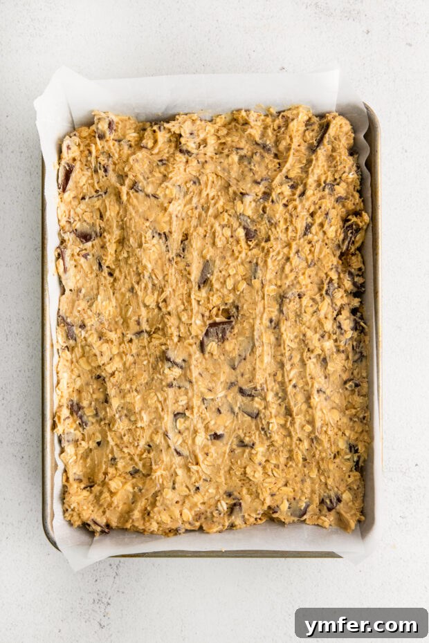 Ultimate Chocolate Chunk Oatmeal Bars 4 Unbaked Chocolate Chunk Oatmeal Cookie Bar dough pressed evenly into a quarter sheet pan, ready for the oven.