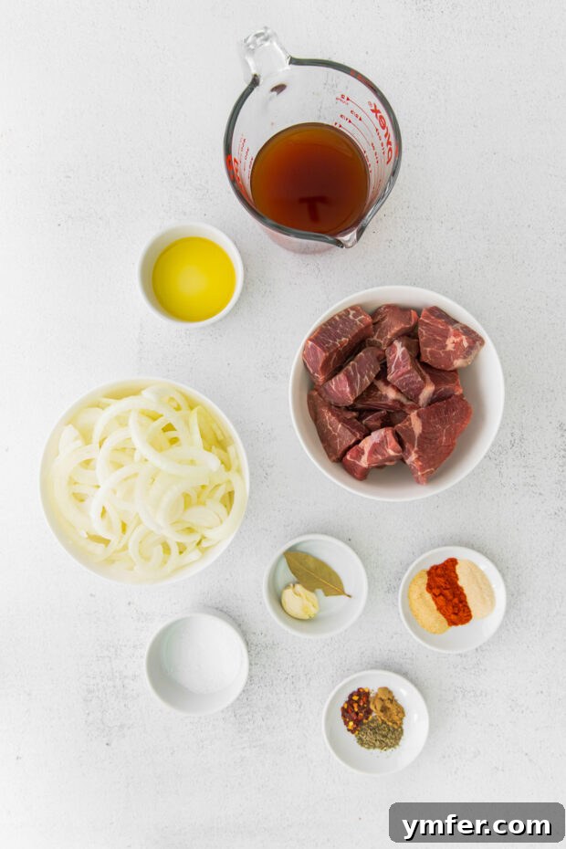 Melt-in-Your-Mouth Slow Cooker Beef Barbacoa 3 Fresh ingredients for Slow Cooker Beef Barbacoa, including cubed chuck roast, onions, garlic, and an array of spices, neatly arranged on a rustic wooden table.