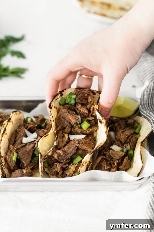 Melt-in-Your-Mouth Slow Cooker Beef Barbacoa 5 A hand holding a warm tortilla filled with shredded Slow Cooker Beef Barbacoa, topped with fresh cilantro and diced red onions, ready to eat.