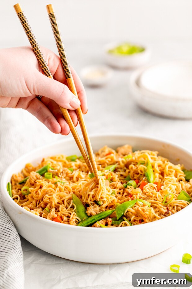 Umami Chicken Ramen Stir Fry 9 A hand using chop sticks picking up ramen noodle stir fry.
