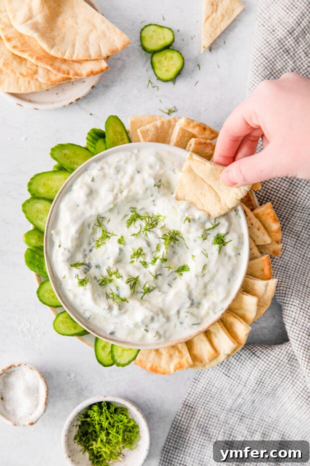 Refreshing Cucumber Yogurt Dip 7 A piece of warm pita bread scooping a generous portion of creamy Tzatziki sauce, highlighting its perfect dipping consistency.