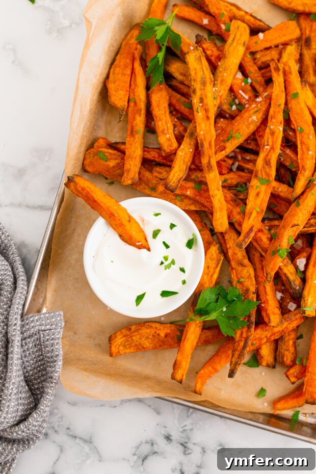 Gourmet Sweet Potato Fries 9 A close-up of a sweet potato fry being dipped into a creamy garlic mayonnaise sauce, highlighting its golden exterior.
