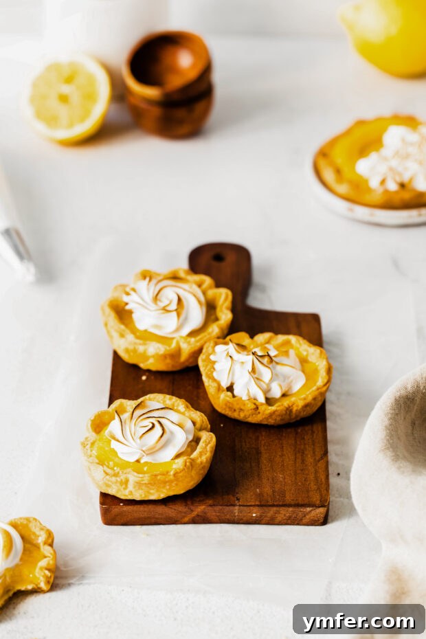 Cloud-Kissed Lemon Tartlets 12 A batch of mini lemon meringue tarts, freshly topped with a swirl of fluffy, untasted meringue on a cutting board.