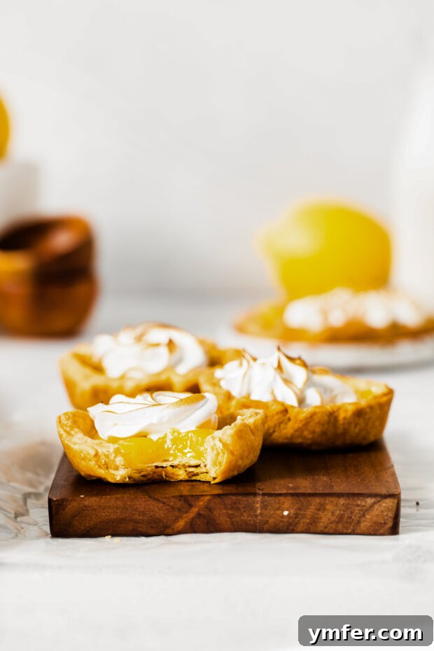 Cloud-Kissed Lemon Tartlets 14 A close-up of a mini lemon meringue tart with a bite taken out, revealing the creamy lemon curd and fluffy meringue inside.