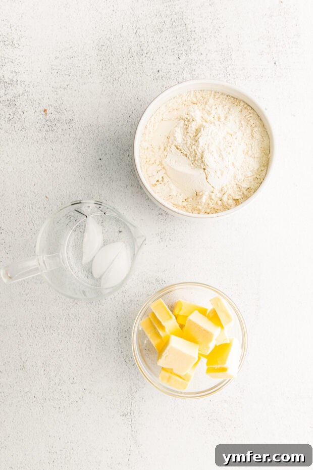 Cloud-Kissed Lemon Tartlets 3 Fresh ingredients for homemade pastry, including butter, flour, and a glass of ice water, laid out on a kitchen counter.