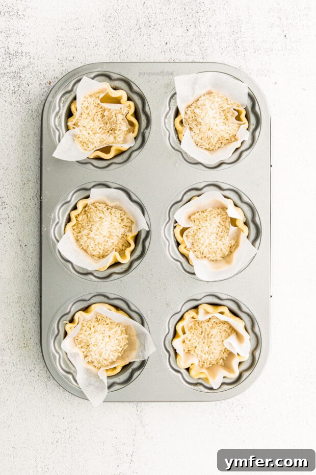 Cloud-Kissed Lemon Tartlets 10 Mini tart shells being blind baked with parchment paper and rice acting as pie weights, ensuring a crisp, even crust.