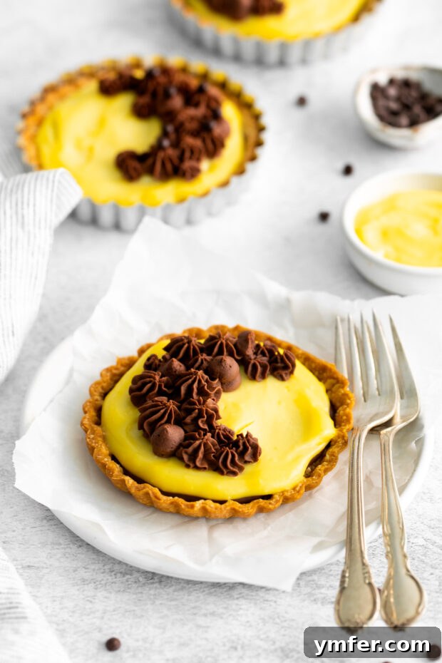 Mini Boston Cream Delights 11 Boston Cream Pie Tarts elegantly arranged on a plate with serving forks, inviting a taste.
