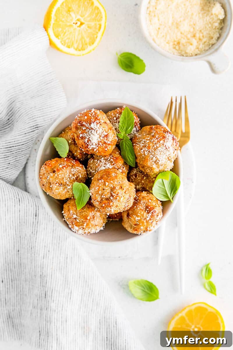 Crispy Air Fryer Chicken Meatballs 2 Air Fryer Chicken Meatballs in a white serving bowl, garnished with fresh herbs and a sprinkle of parmesan cheese.