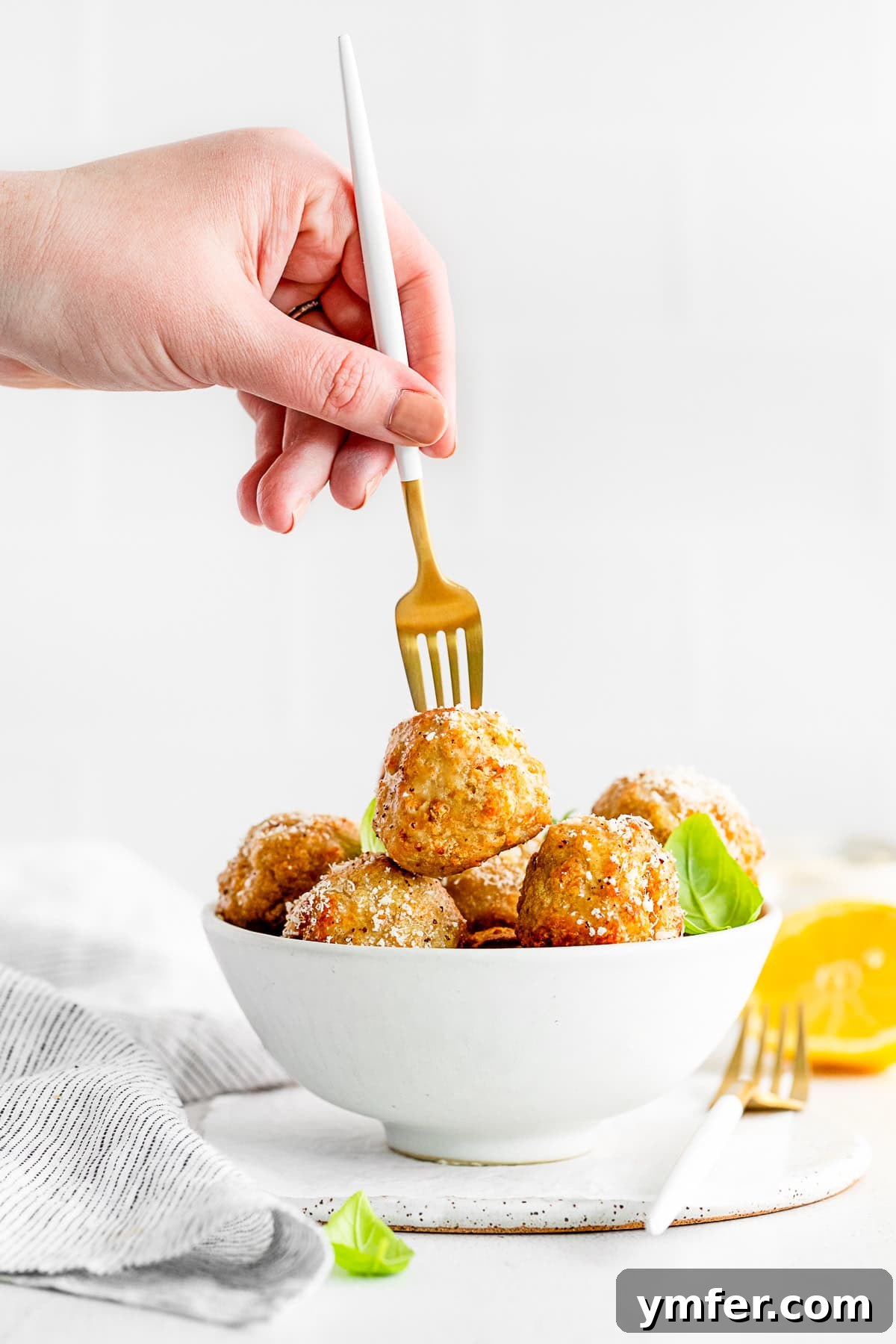 Crispy Air Fryer Chicken Meatballs 8 A fork picking up a golden-brown Air Fryer Chicken Meatball from a white serving plate, showing its texture.