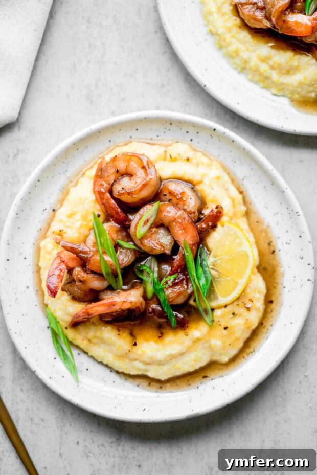 Cajun Honey Butter Shrimp with Creamy Grits 2 Cajun Honey Butter Shrimp and Grits on a white serving plate, garnished with fresh herbs.