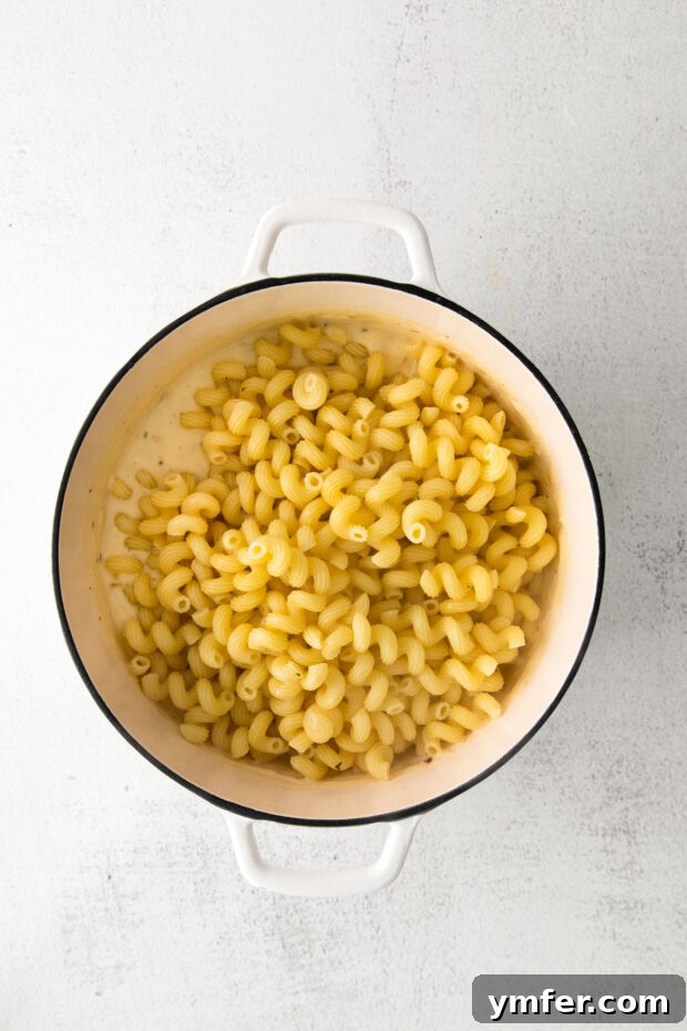 Creamy White Cheddar Mac 6 White Cheddar Mac and Cheese being stirred in a large Dutch oven, showing the creamy sauce coating the pasta.