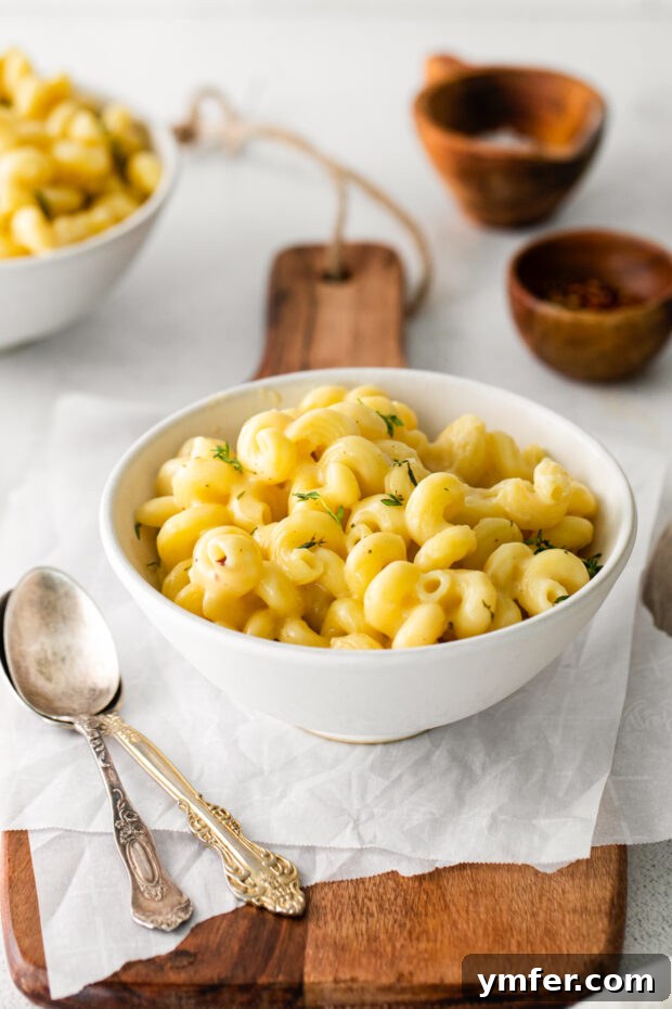 Creamy White Cheddar Mac 7 A perfectly portioned serving of White Cheddar Mac and Cheese in a white bowl, garnished with a sprig of fresh thyme.