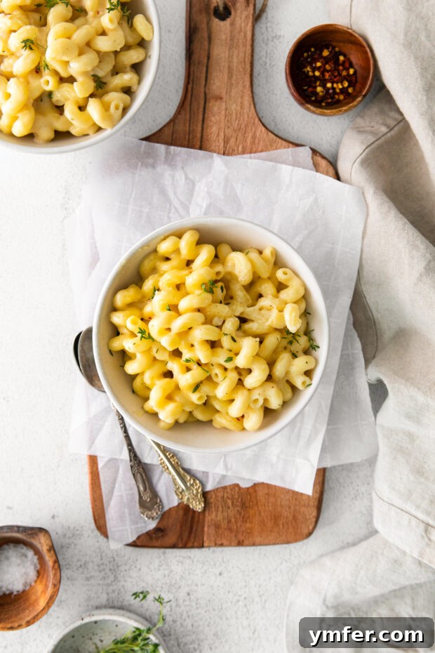 Creamy White Cheddar Mac 8 A close-up of White Cheddar Mac and Cheese, freshly made and topped with delicate sprigs of fresh thyme, highlighting its creamy texture.