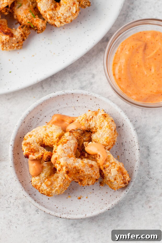 Golden Crispy Air Fryer Shrimp 10 Crispy Air Fryer Shrimp drizzled with a homemade spicy mayo, presented beautifully on a plate.