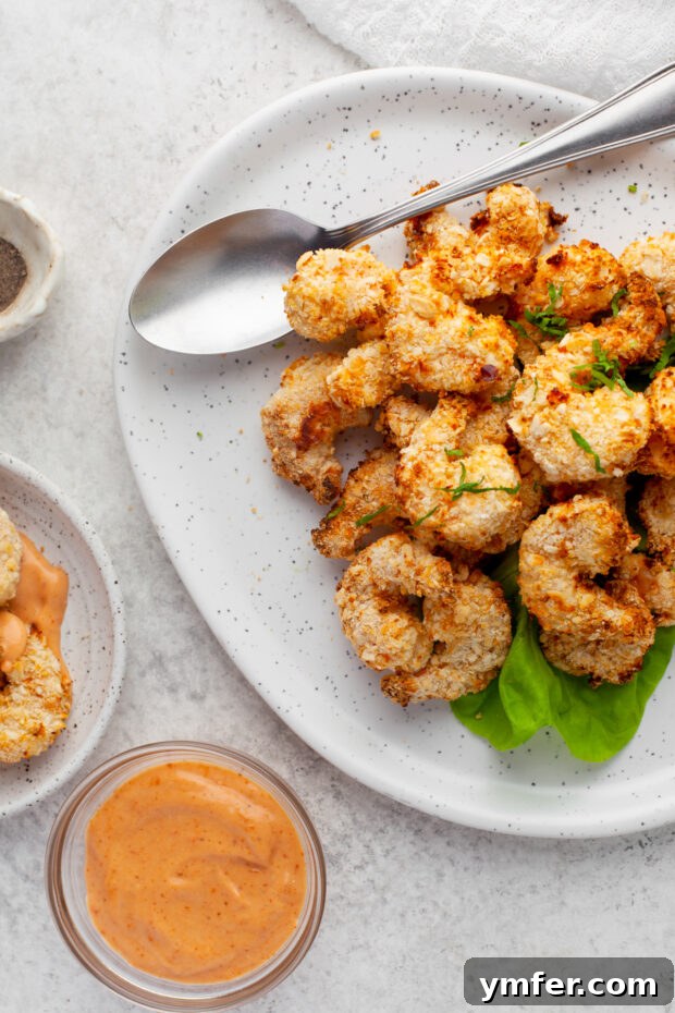 Golden Crispy Air Fryer Shrimp 11 Crispy Air Fryer Shrimp on a plate with a side of creamy dipping sauce, ready to be enjoyed.