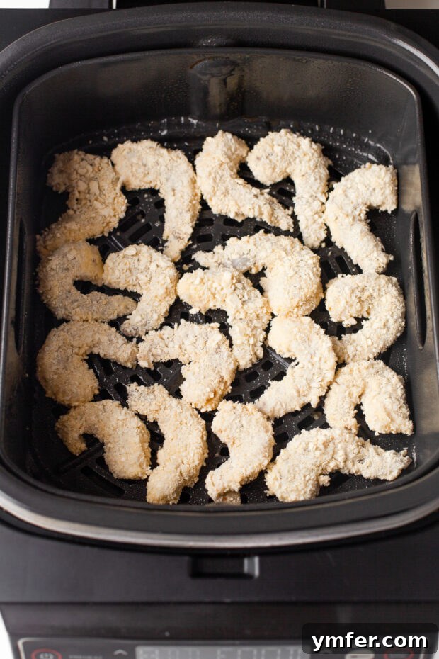Golden Crispy Air Fryer Shrimp 7 Breaded shrimp arranged in a single layer in an air fryer basket, uncooked and ready for cooking.
