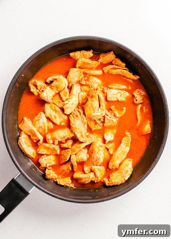Zesty Buffalo Chicken Wrap 3 Chicken strips cooking in buffalo sauce marinade in a skillet.