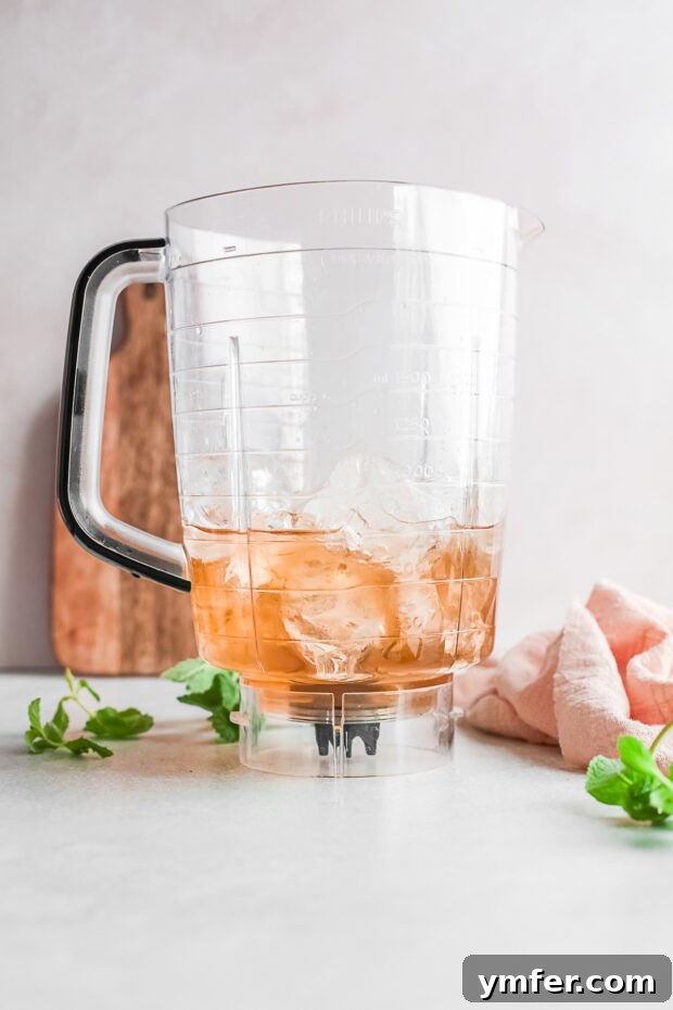 Kentucky Mint Slush 3 High-quality bourbon and ice cubes being added into a blender, beginning the process of making a frozen mint julep.