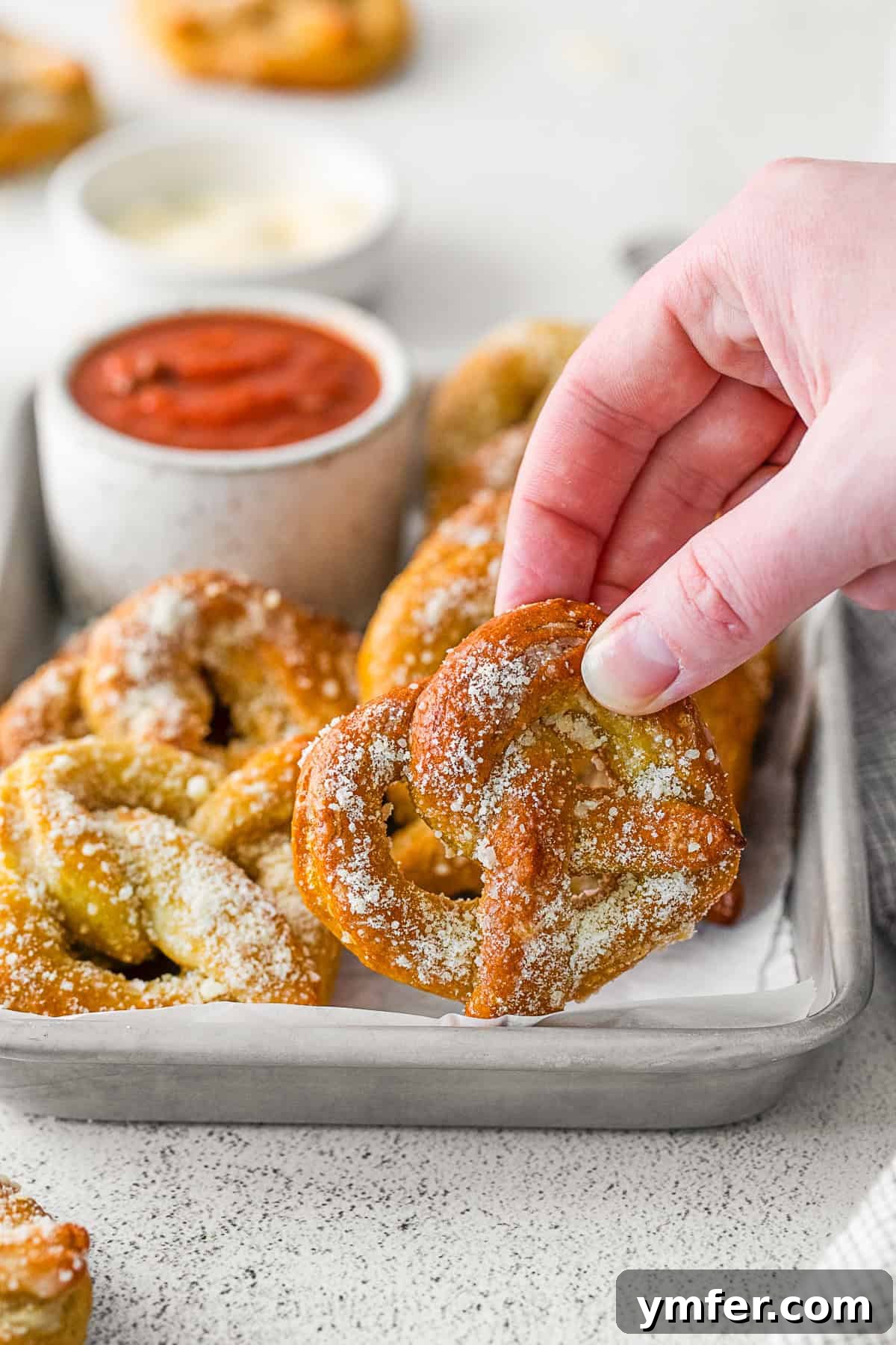 A hand gently holding a warm, freshly baked garlic parmesan soft pretzel, showcasing its golden crust and savory topping.