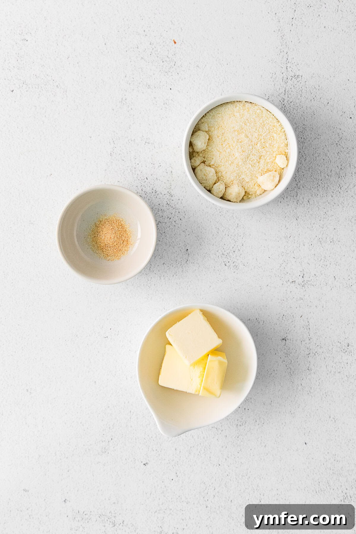 Ingredients for the garlic parmesan topping, including melted butter, grated parmesan cheese, and garlic powder, on a clean surface.
